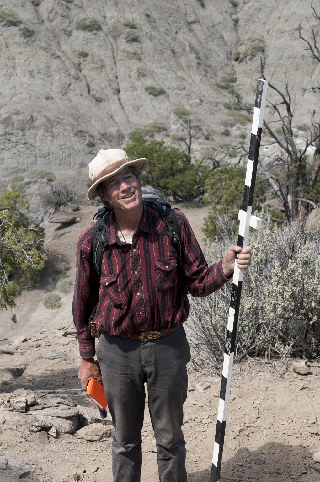Dr. Bob Raynolds, DMNS Research Associate, holds a survey pole in one hand and his field journal in the other as he looks up at their most recent find.